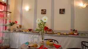 Un buffet de petit-déjeuner proposant divers plats, un vase rempli de fleurs blanches et une table dressée avec des assiettes, des couverts et une serviette rouge.