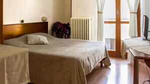 Une chambre d’hôtel avec deux lits, un radiateur, un bureau avec un ordinateur et une fenêtre avec des rideaux.