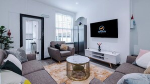 A modern living room with a grey sofa set, a round coffee table, and a flat-screen TV mounted on the wall.