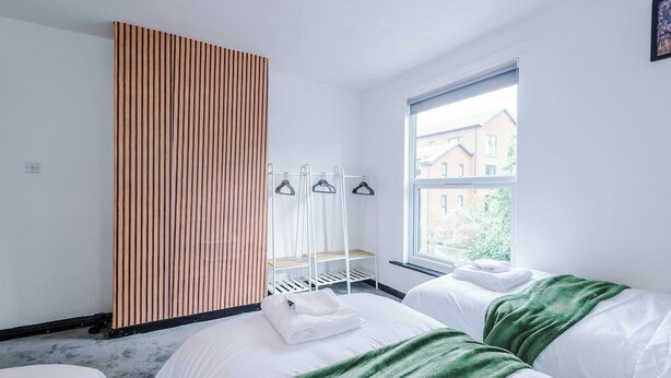 A hotel room with two beds, a wooden panel wall, a window with a view of buildings, and a drying rack with clothes.