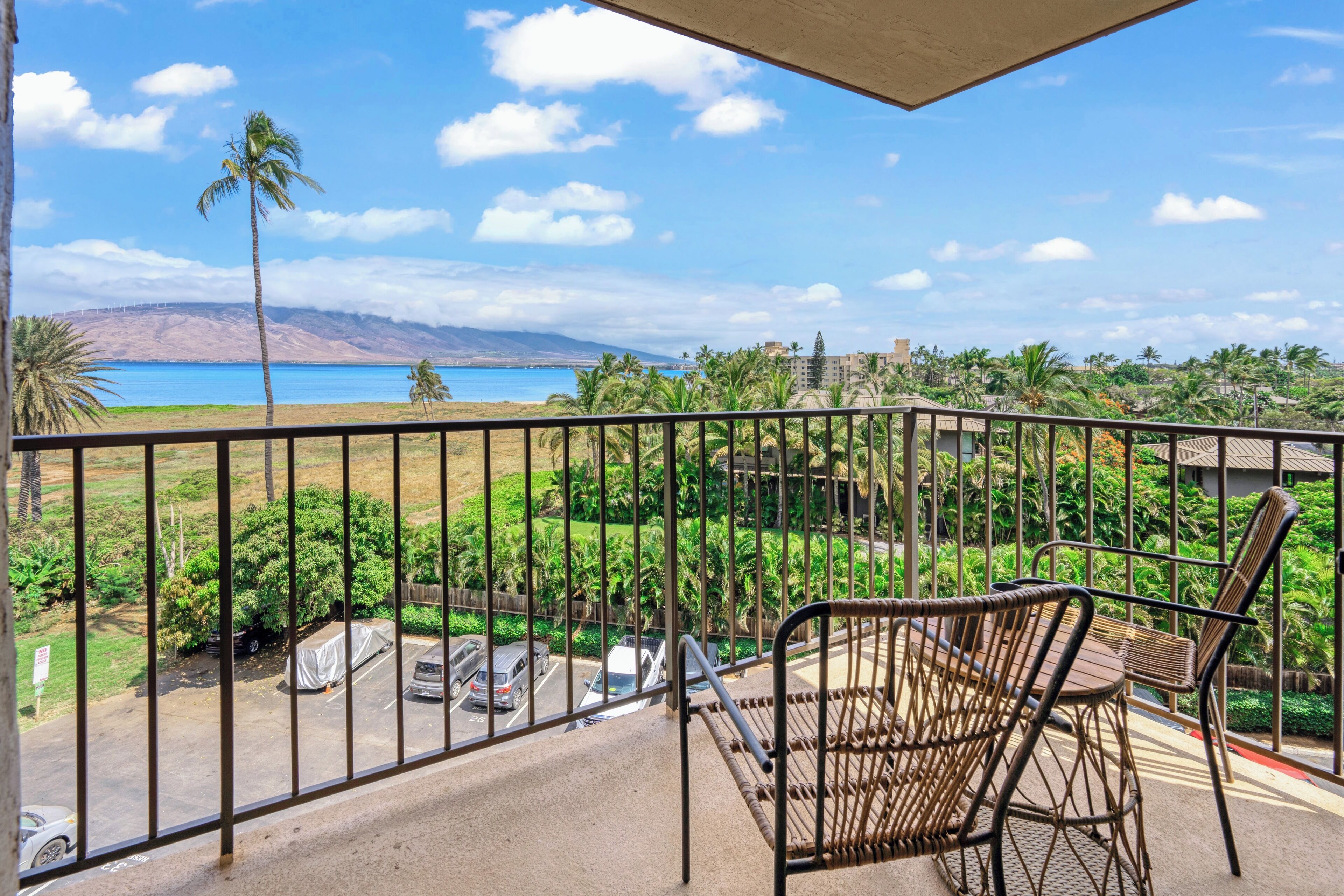 Ein Balkon mit Korbmöbeln, mit Blick auf einen Strand und einen Parkplatz.