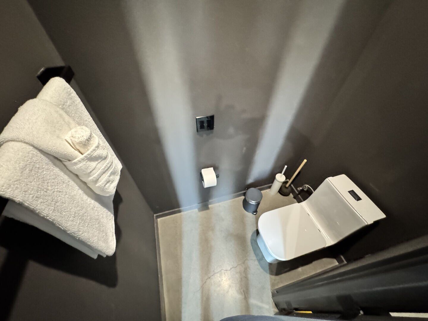 A bathroom with a white towel hanging on the wall, a toilet paper dispenser, and a sink.