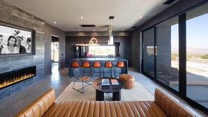 A modern kitchen with a central island, a fireplace, and a dining area with leather seating. - Black Casita by Fieldtrip - Bold Villa w Pool + Spa (Joshua Tree)