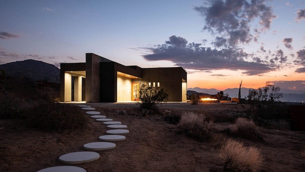 A modern house with a concrete exterior, a paved pathway leading to the entrance, and a desert landscape in the background. - Black Casita by Fieldtrip - Bold Villa w Pool + Spa (Joshua Tree)