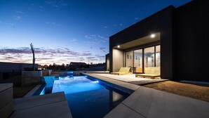 A modern outdoor pool area with a clear view of the sky and a building with large windows. - Black Casita by Fieldtrip - Bold Villa w Pool + Spa (Joshua Tree)