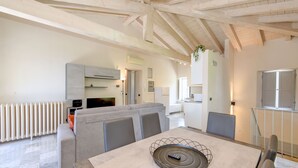 A spacious living area with a high ceiling, a dining table with chairs, a sofa, and a kitchen in the background.