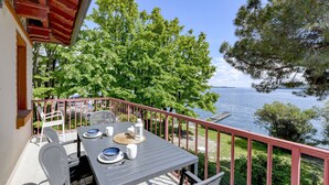 A balcony with a table set for dining, overlooking a lake with trees and a clear sky.