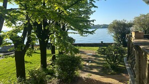 A pathway leading to a lake with trees and a stone wall on the right.