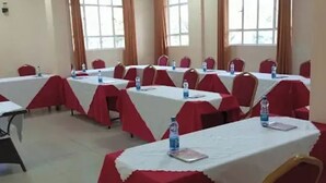 A conference room with tables covered in white tablecloths and red chair covers, equipped with water bottles. - Fairways Hotel (Narok)