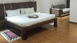 A bedroom with a wooden bed, a nightstand, a bedside table, a chair, and a small table with a book. - Fairways Hotel (Narok)