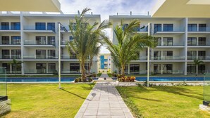 A modern hotel with a central pool, multiple balconies, and a well-maintained lawn. - Tropical 2BR Retreat - Terrace, BBQ and Pool (Punta Cana)
