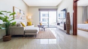 A modern hotel room with a sofa, a small table, a lamp, a large potted plant, and a view of the outside. - Tropical 2BR Retreat - Terrace, BBQ and Pool (Punta Cana)