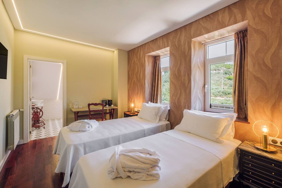 A hotel room with two beds, a desk, a chair, and a window with curtains.