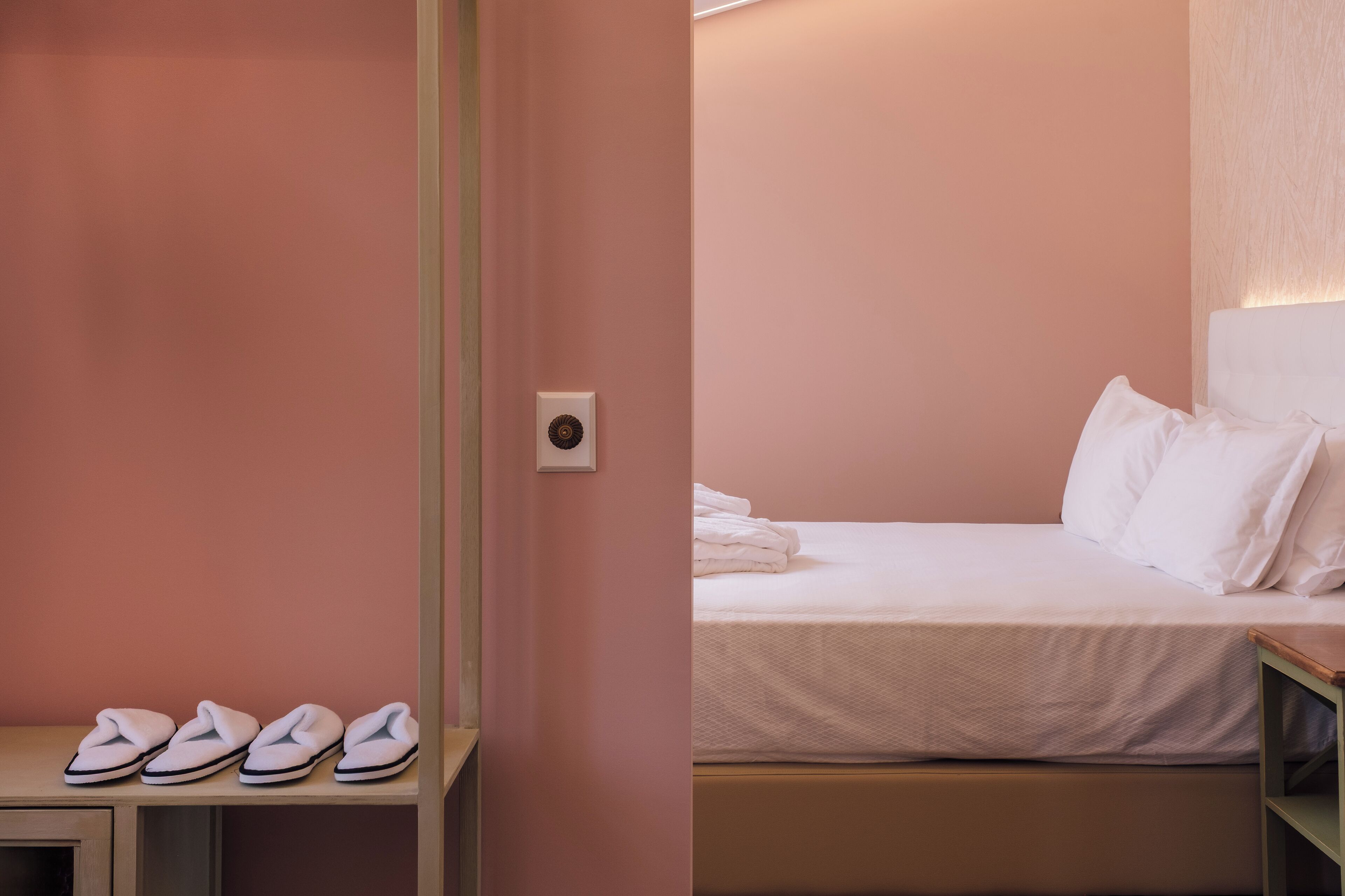 A bedroom with a bed, pillows, a bedside table, and a pair of slippers.