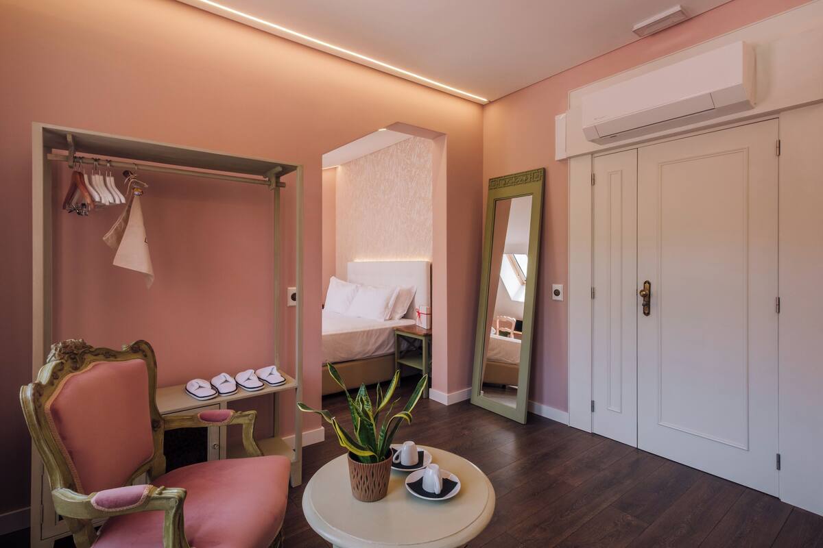 A hotel room with a bed, a chair, a table with a plant, and a mirror.