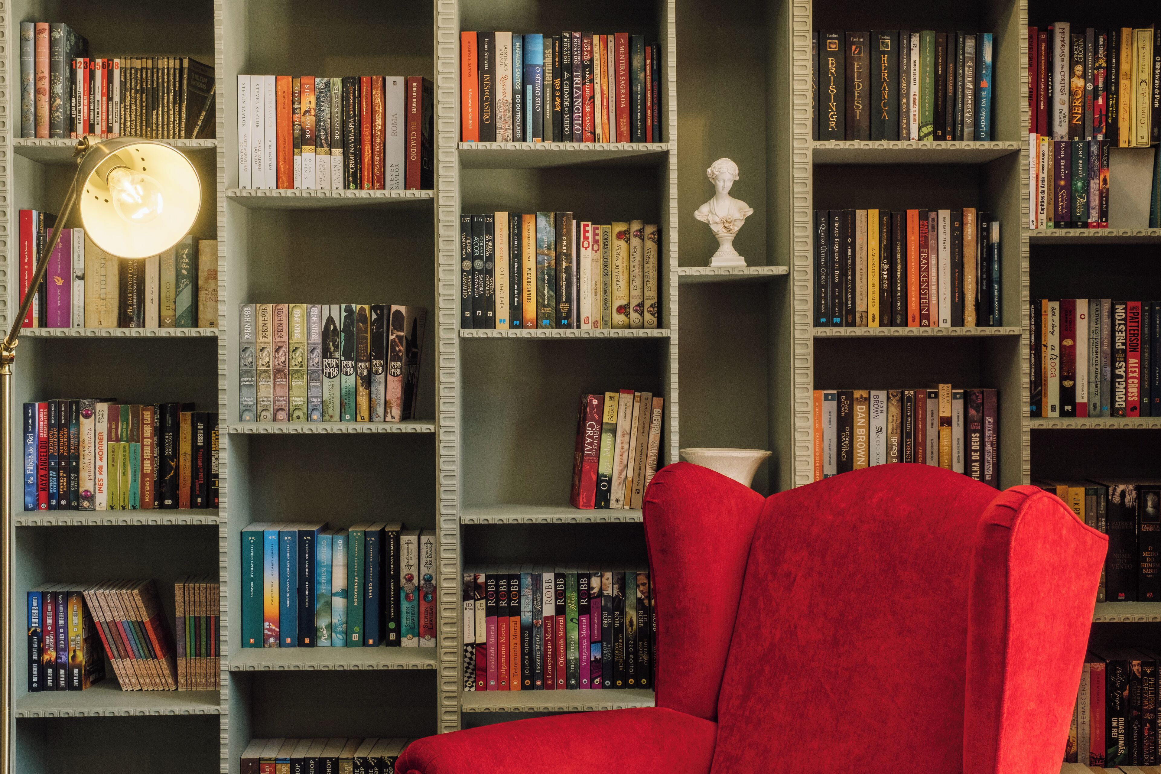 Una biblioteca con estanterías llenas de libros, una silla roja y una lámpara de escritorio.