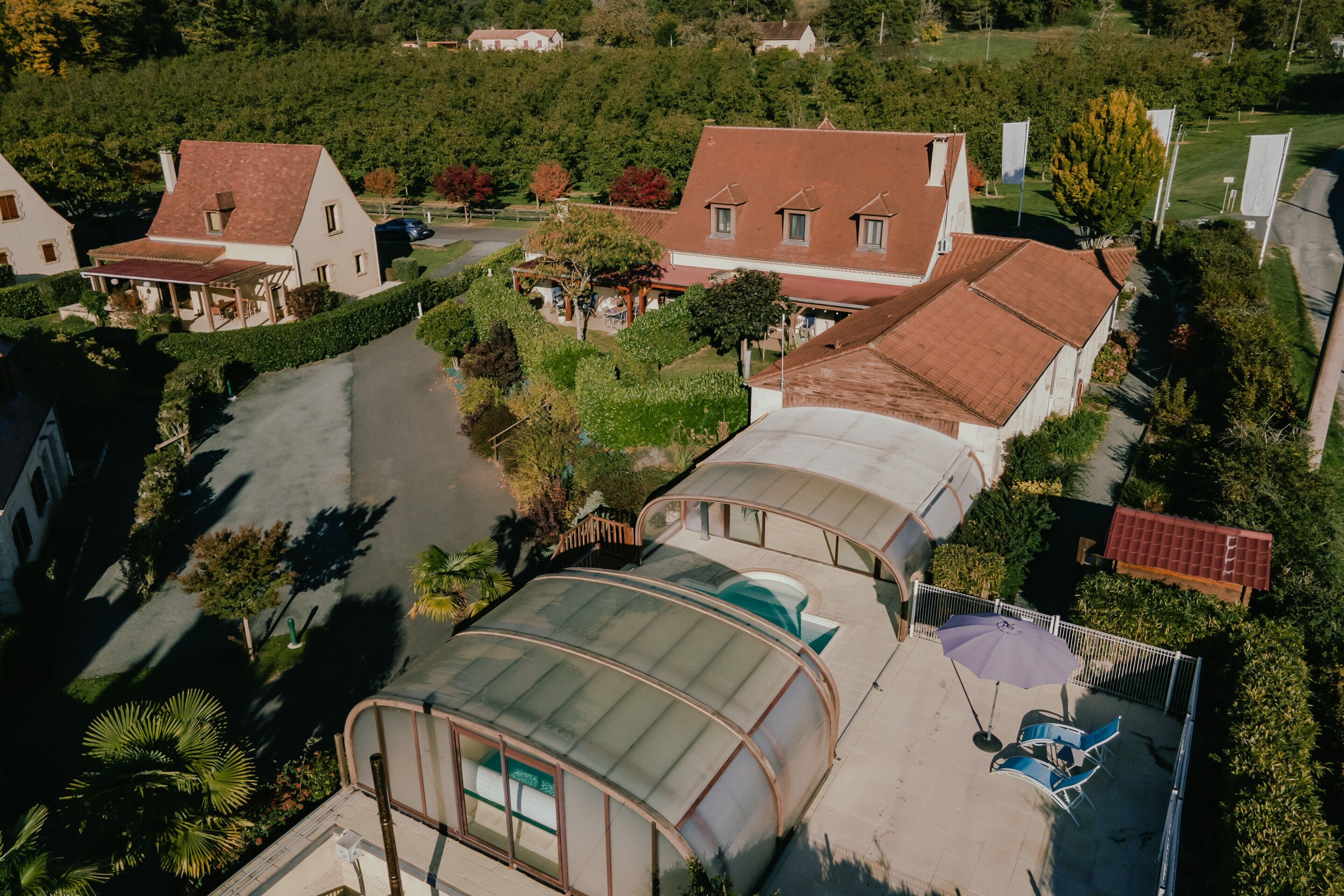 Un quartier résidentiel avec des maisons, une serre et une terrasse clôturée, aménagée avec des chaises et un parasol.