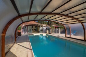 Ein überdachter, innenliegender Pool mit gewölbter Dachkonstruktion, Glaswänden und Fliesenboden.