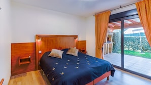 Un dormitorio con cama, cabecero de madera y vistas a un jardín a través de un ventanal corredero.