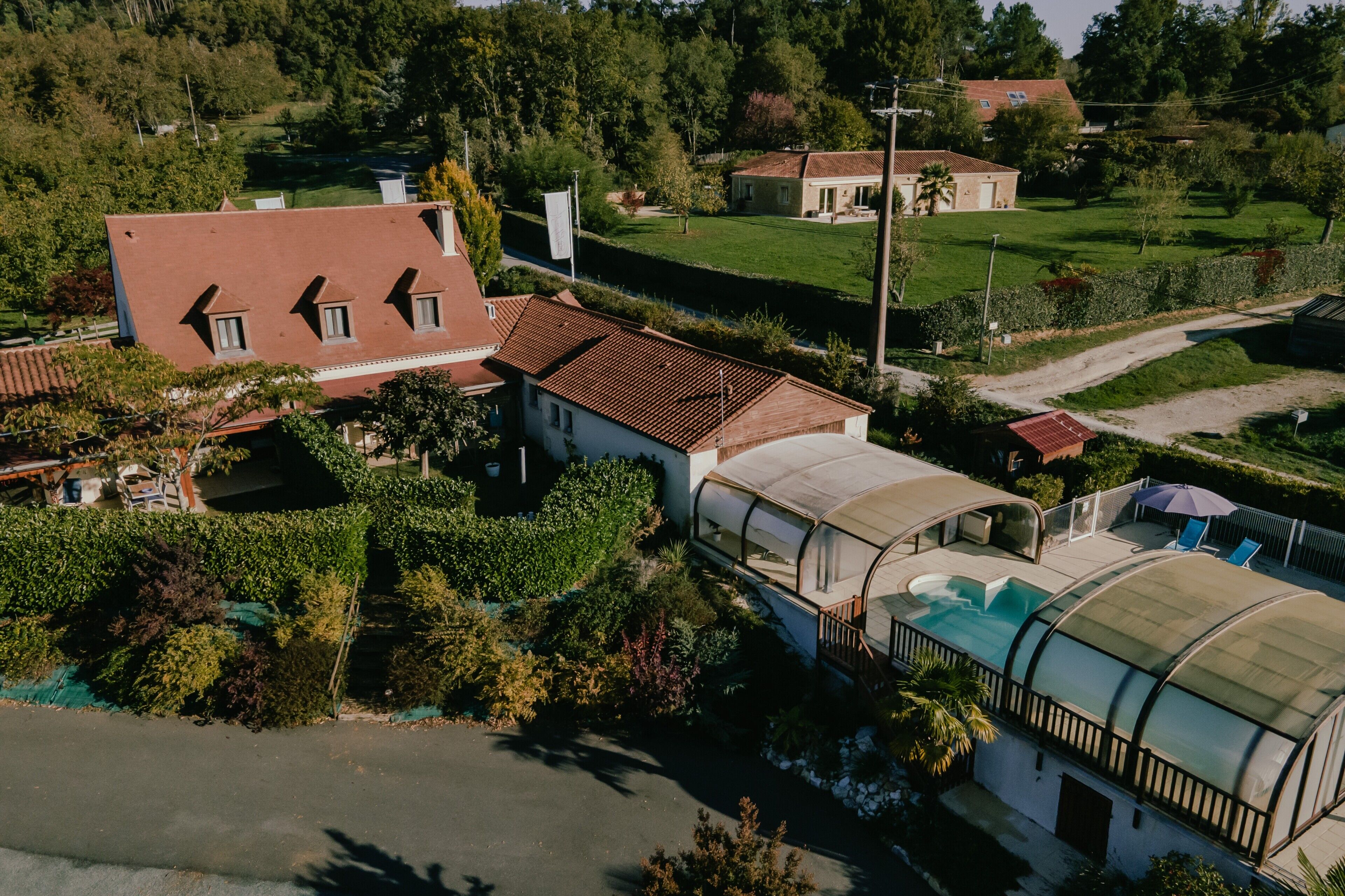 A house with a large garden, a swimming pool with a glass enclosure, and a red-roofed building.