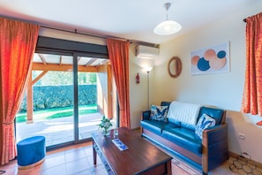 Un salon avec un canapé, une table basse et une vue sur l’extérieur, visible à travers une porte vitrée.