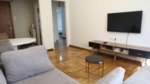 A modern living room with a sofa, a coffee table, and a TV mounted on the wall. - Serene & Stylish Apt Athens – Exarcheia by GHH (Athens)