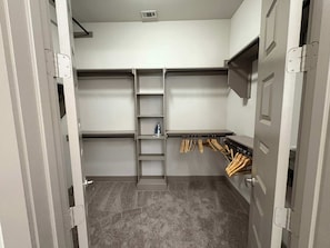 Ein begehbarer Kleiderschrank mit offenen Regalen, einer Kleiderstange und einem kleinen Bügelbrett.