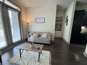 Ein Wohnzimmer mit grauem Sofa, Couchtisch, Stehlampe und einer Wand mit einem gerahmten Zitat.