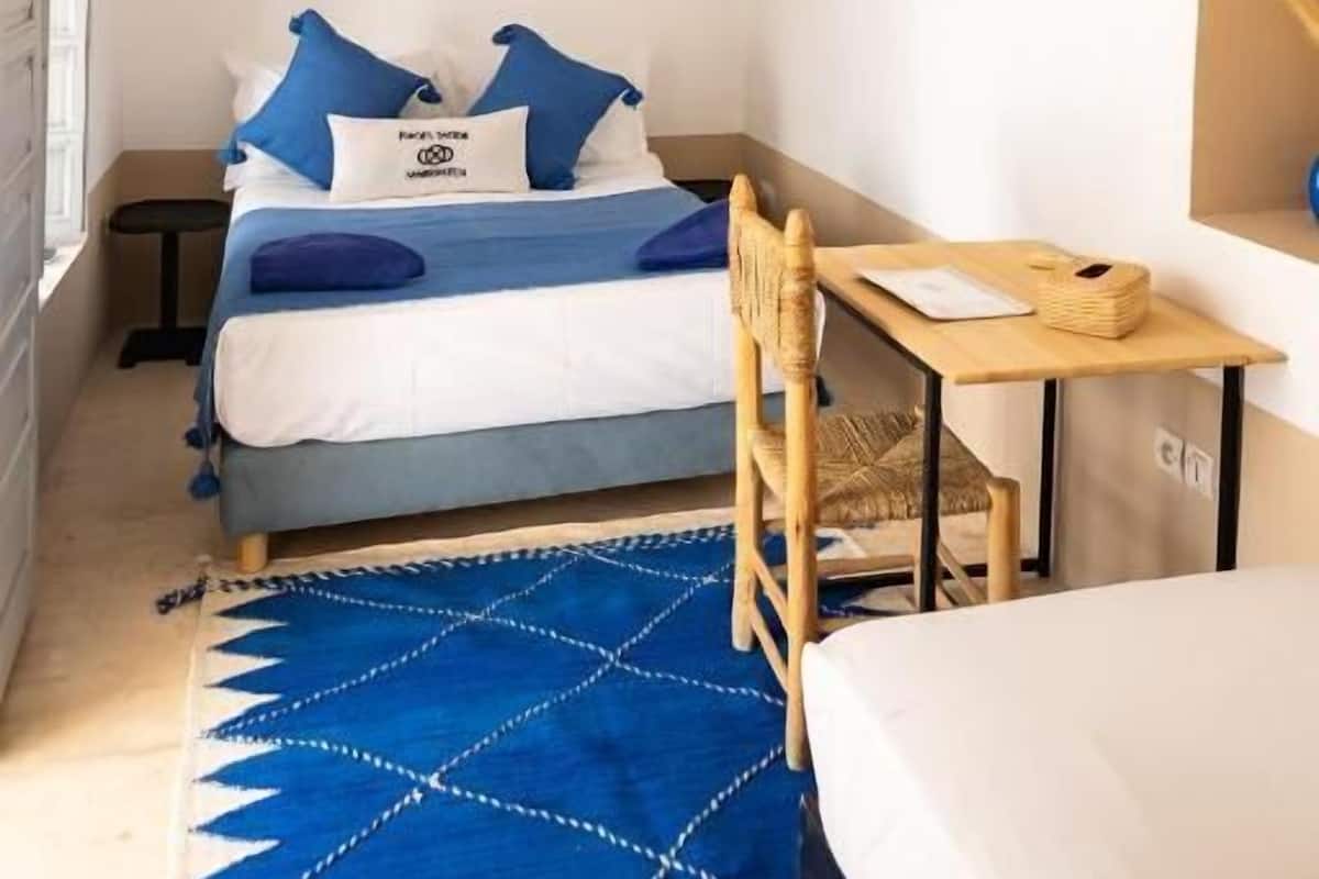 A bedroom with a bed, a desk, and a chair. There are wall decorations and a hanging light fixture.