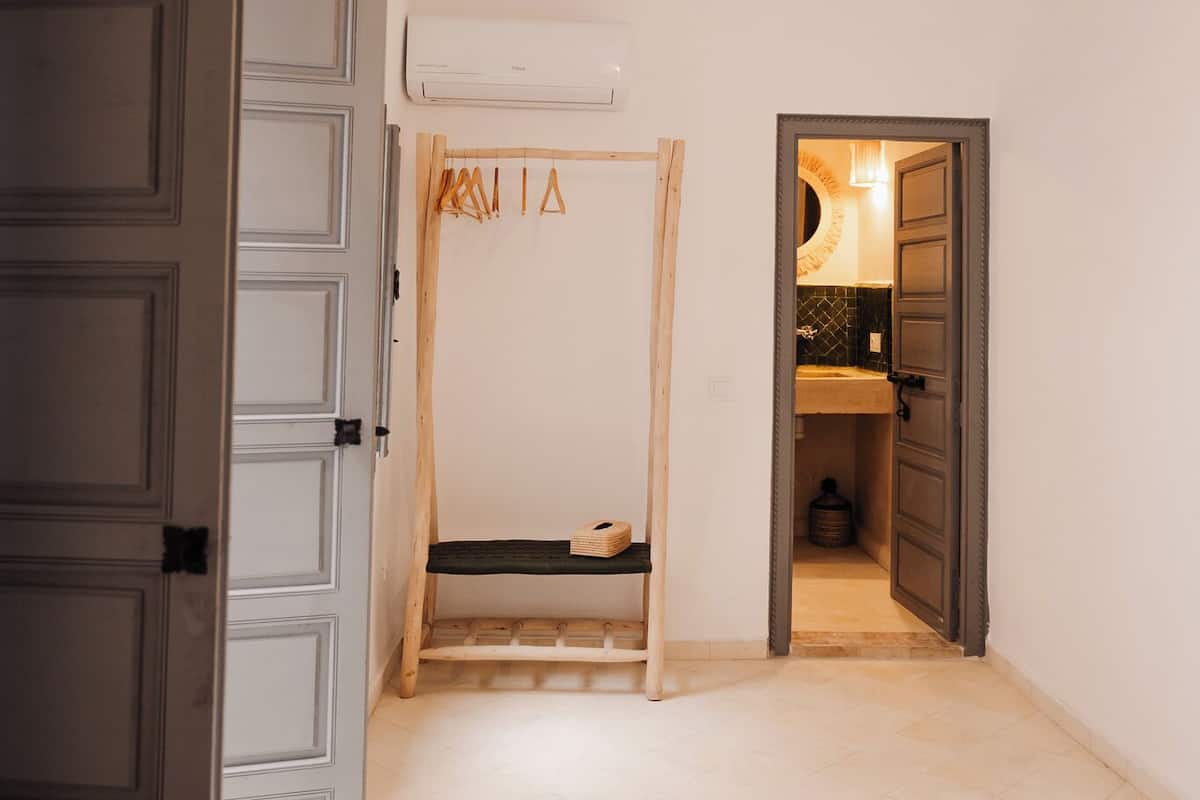 A bedroom with a bed, a wardrobe, a hanging light fixture, and a bathroom visible through an open door.