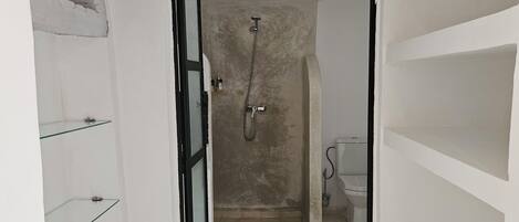 Un pasillo estrecho que conduce a un baño con ducha, inodoro y estantes de vidrio a la izquierda.
