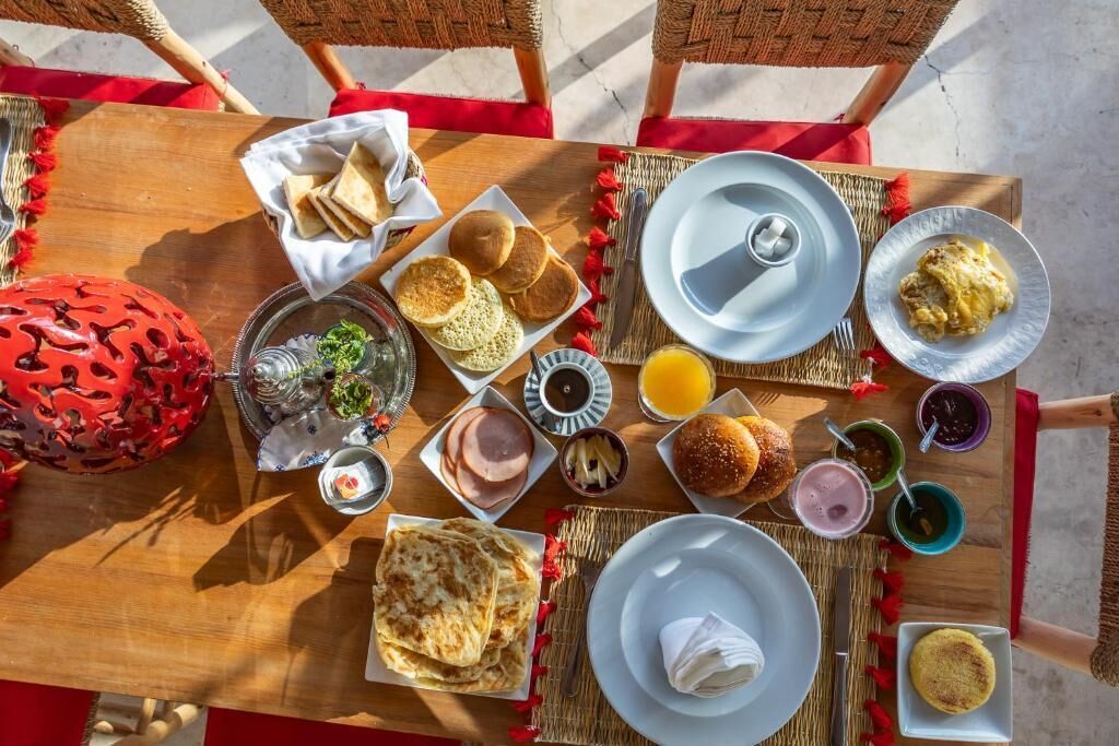 A breakfast table with various dishes including pancakes, eggs, and toast, set on a wooden table with woven placemats.