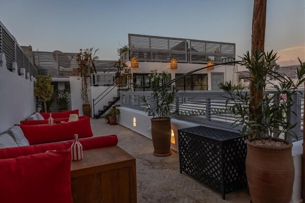 A rooftop terrace with red cushioned seating, potted plants, and a staircase leading to an upper level. - Riad El Jadide (Marrakech)