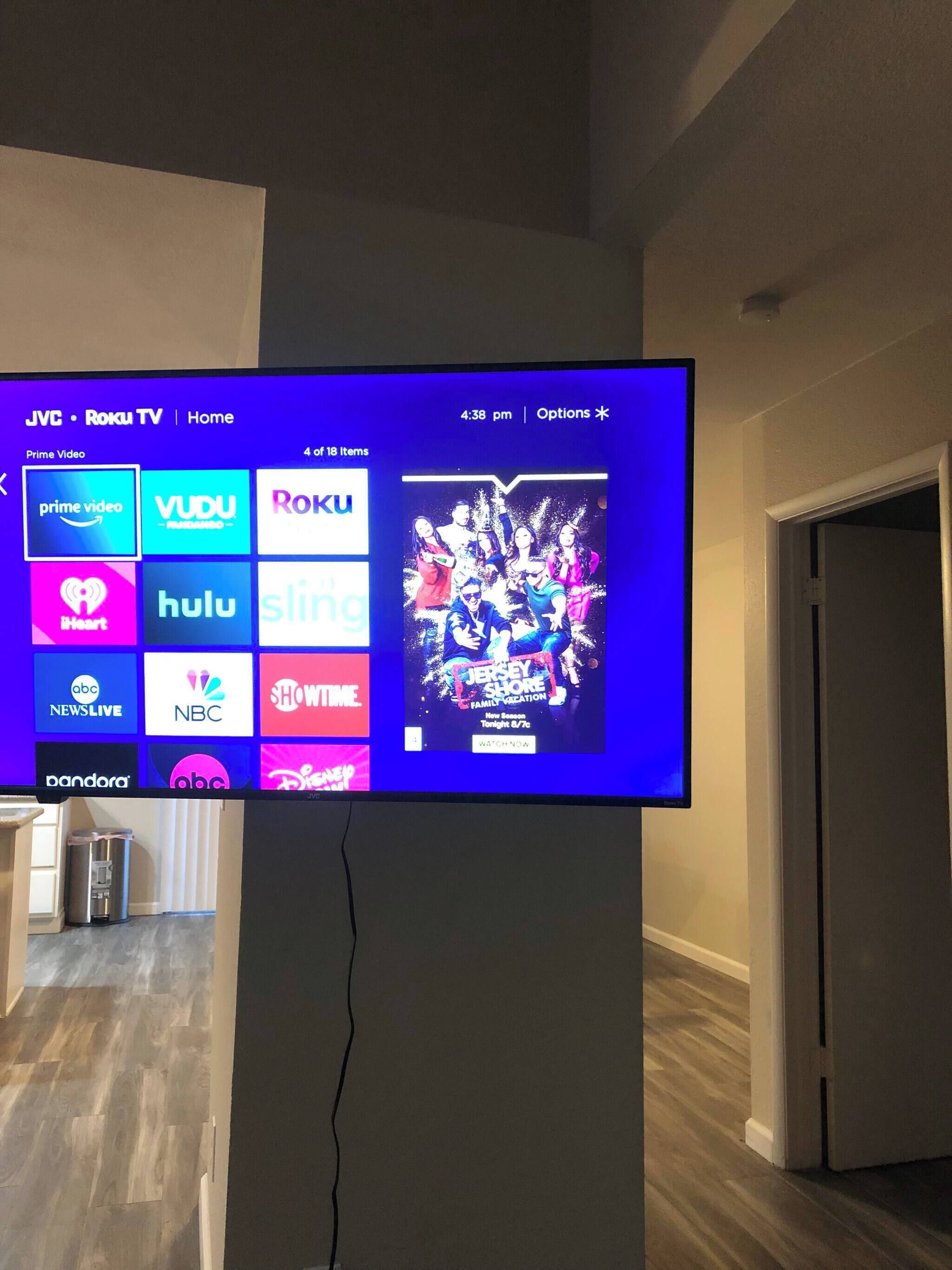 Ein Flachbildfernseher an der Wand zeigt eine Streaming-Dienstanzeige mit verschiedenen Kanal-Logos und einem Filmplakat.