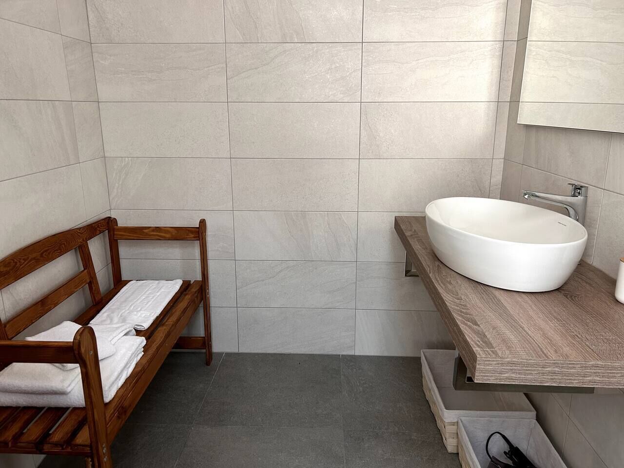Une salle de bain avec un banc en bois, un grand lavabo et des murs carrelés.