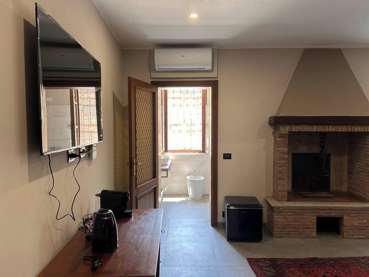 Ein Zimmer mit flachbildfernseher an der Wand, Kamin, Fenster mit Blick und Fliesenboden.