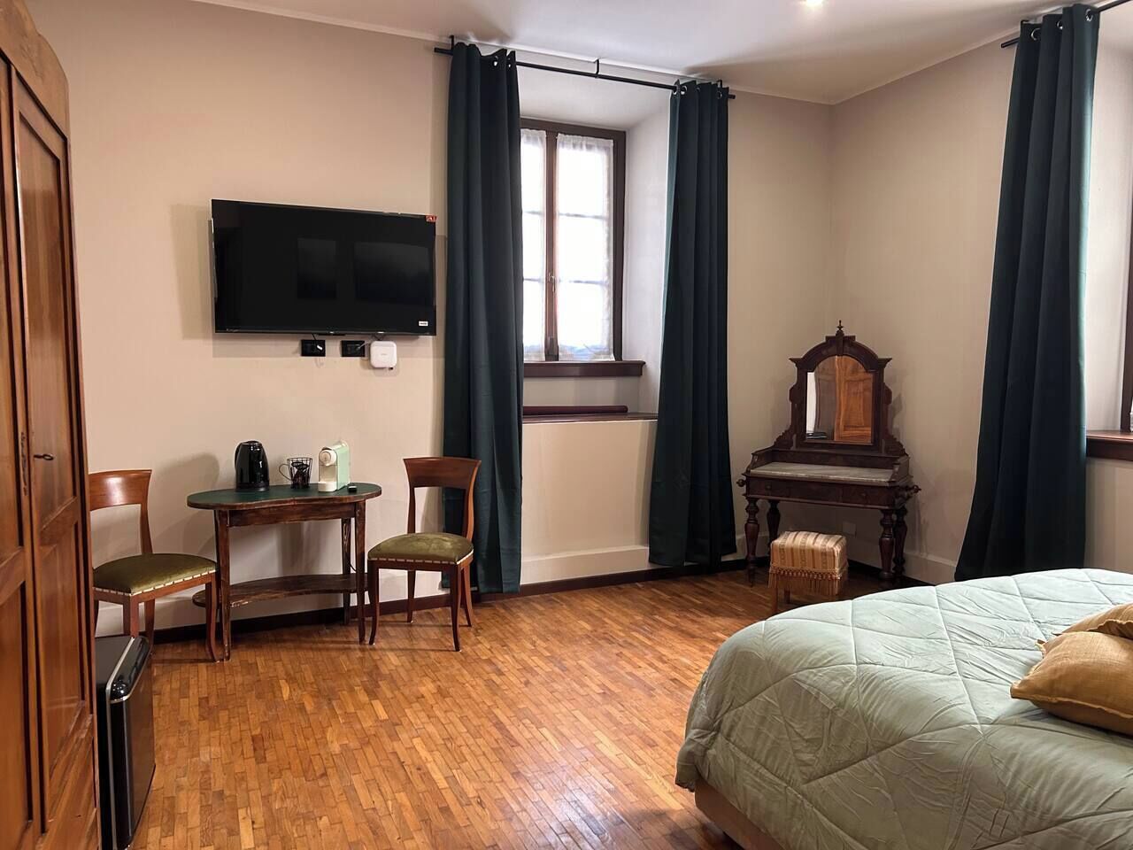 A hotel room with a bed, a desk with a chair, a television, a wooden dresser, and a window with curtains.