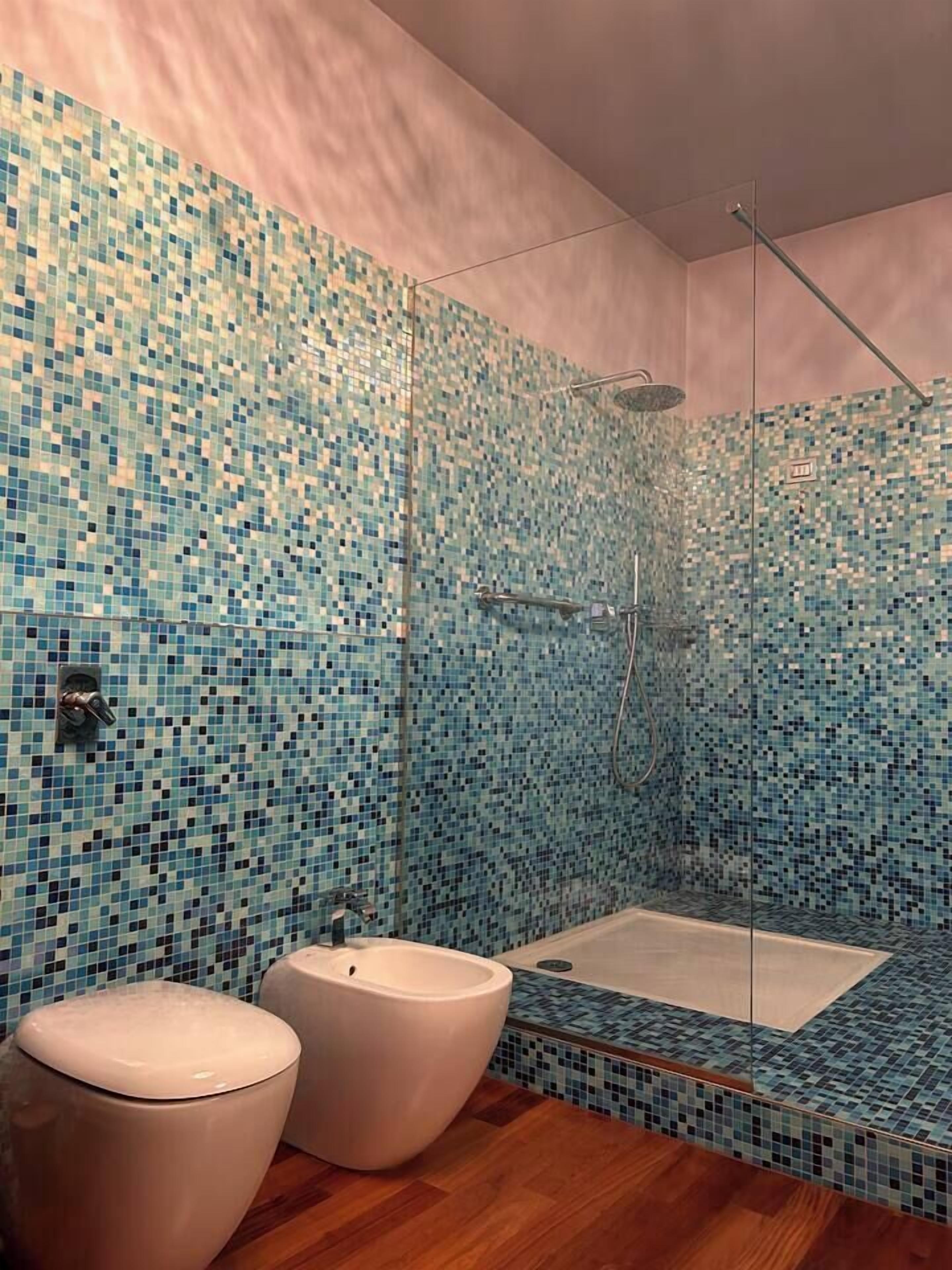 Une salle de bain avec des murs recouverts de mosaïques, une douche en verre et un plancher en bois.