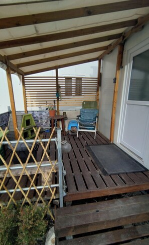 Ein überdachter Außenbereich mit Holzterrasse, einem Sessel, einem kleinen Tisch und einem Blumentopf.