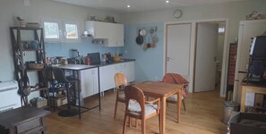 A compact kitchen with white cabinets, a dining table, and chairs. There is a small shelf with jars and a kettle.
