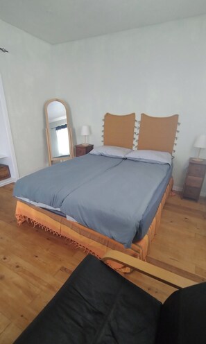A bedroom with a bed, a nightstand, a lamp, a mirror, and a wooden floor.