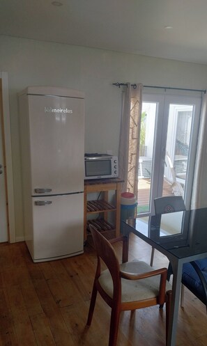 A compact kitchen with a refrigerator, a microwave, a small table, and a chair.
