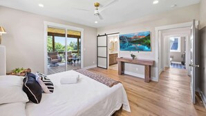 A bedroom with a bed, a desk, a painting, and a sliding door leading to a balcony.
