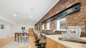 Una cocina moderna con pared de ladrillo, taburetes de bar de madera y una zona de comedor con mesa y sillas.
