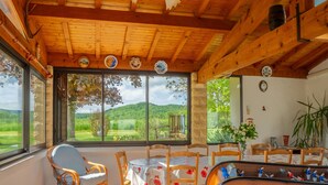 A dining area with a pool table, wooden chairs, and large windows offering a view of the countryside.
