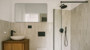 Un baño moderno con un lavamanos independiente, un inodoro, una ducha con manguera negra y un espejo sobre el lavamanos.