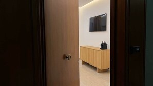 Un interior moderno con una puerta de madera, piso de color claro, un armario de madera y un bolso negro sobre el armario.