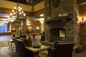 A lobby with a stone fireplace, leather seating, chandeliers, and a high ceiling. - Modern-Rustic Retreat + Full Kitchen, Soaking Tub, Office, Media Room & Deck (Whitefish)