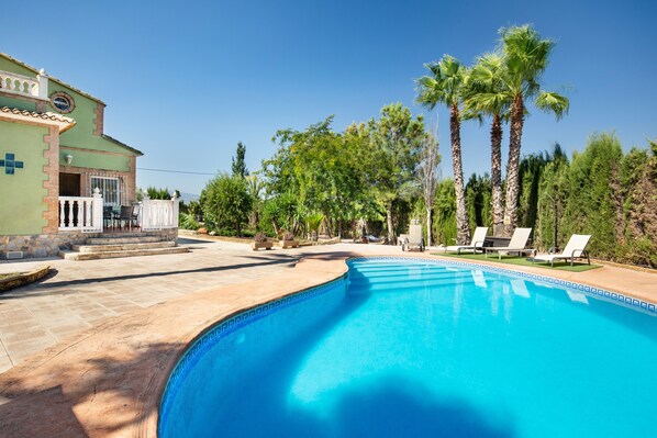 A swimming pool with lounge chairs, palm trees, and a building with a green facade.