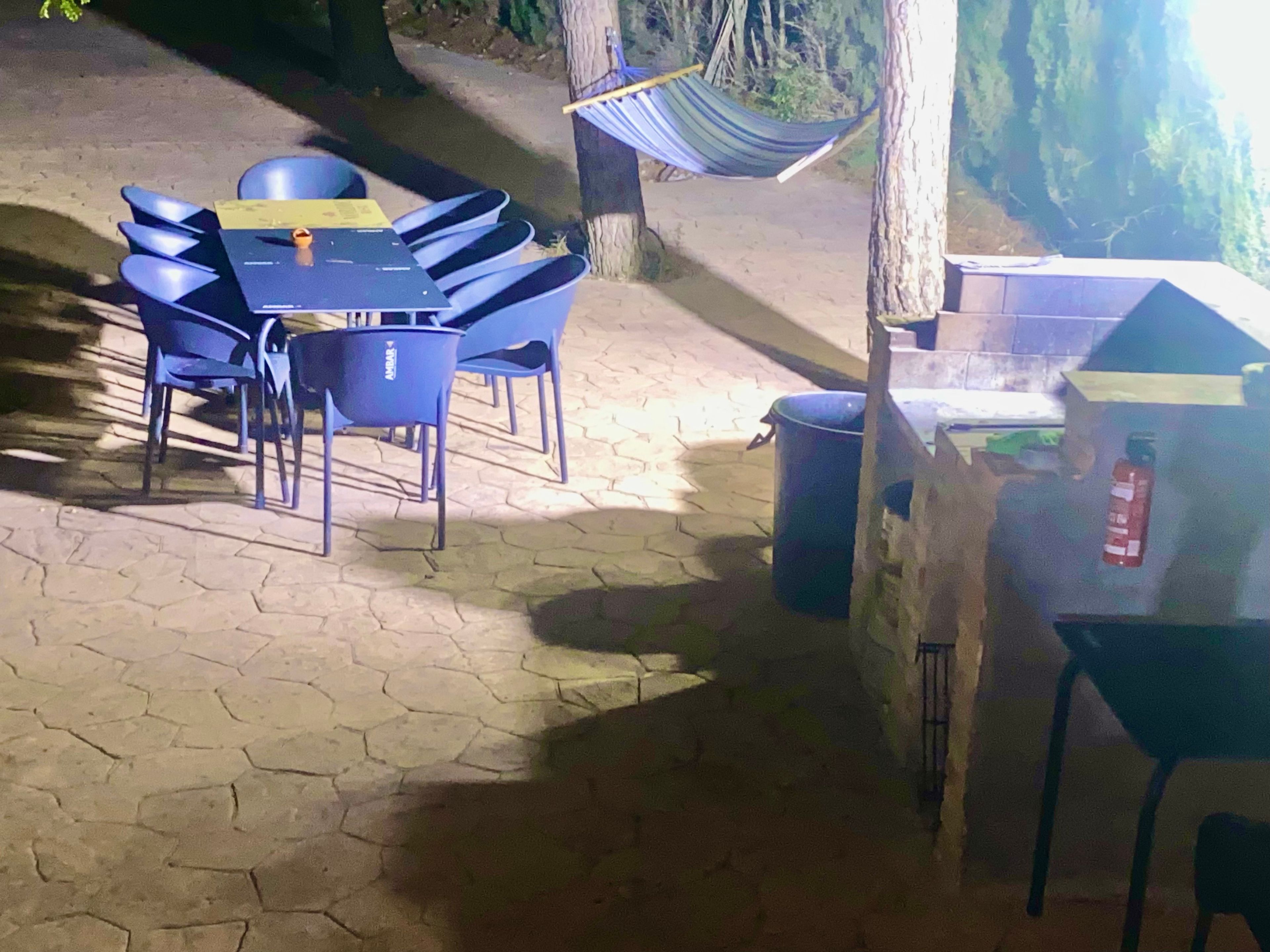 An outdoor seating area with tables and chairs, a hammock, and a trash bin.